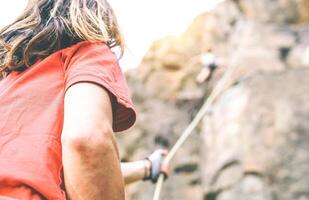 Woman climbing up on mountain cliff while man helping her to climb to the top holding the rope - Climber in action on the rock near the peak - Ambition, adrenaline, sport concept photo