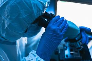 joven científico trabajando en laboratorio examinando coronavirus mediante microscopio - Ciencias y tecnología concepto foto