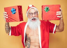 Tattooed fit santa claus holding christmas gifts - Trendy bearded hipster senior wearing xmas clothes showing presents - Concept of celebration culture and x-mas holidays concept photo