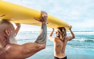 Happy fit friends having fun surfing on tropical ocean - Surfers father and son doing stretching surf exercises - Sporty people lifestyle and extreme sport concept photo