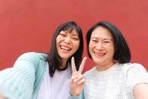 asiático madre y hija tomando selfie con móvil teléfono inteligente al aire libre - contento chino familia teniendo divertido compartiendo en línea fotos para social medios de comunicación - personas padres y tecnología estilo de vida concepto