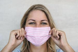 Young woman wearing pink face mask portrait - Blonde female using protective facemask for preventing spread of corona virus - Health care and pandemic crisis concept photo