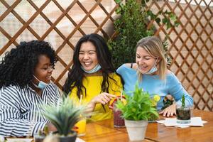 Multiracial friends watching on mobile smartphone while having healthy lunch in coffee brunch bar during corona virus outbreak - Food and technology concept photo