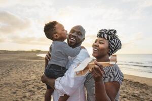 Happy African family having fun on the beach during summer vacation - Parents love and unity concept photo