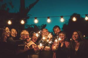 contento familia celebrando con bengala a noche fiesta al aire libre - grupo de personas con diferente siglos y etnia teniendo divertido juntos fuera de - amistad, víspera y celebracion concepto foto