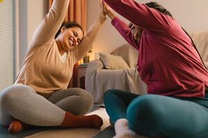 Happy young daughter with her mother having fun doing yoga at home photo