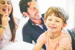 Happy family having fun together on a bed at home - Portrait of a child laughing with lollipop in the living room with his father and sister - Concept of unity, family and love photo