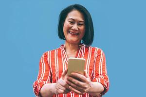 asiático mayor mujer teniendo divertido con móvil teléfono al aire libre - contento chino hembra utilizando teléfono inteligente fuera de - ancianos, sociales, tecnología y personas estilo de vida concepto foto