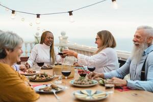 Happy multiracial senior friends having fun dining together on house patio - Elderly lifestyle people and food concept photo
