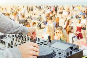 Close up of DJ's hand playing music at turntable at beach party festival - Crowd people dancing and having fun in club outdoor - Concept of youth summer party lifestyle photo