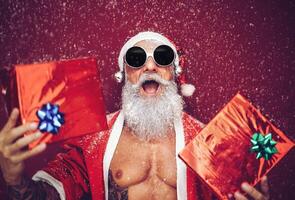 contento ajuste Papa Noel claus riendo y dando Navidad regalos - de moda barba tatuaje hipster mayor vistiendo Navidad ropa y participación regalos - celebracion y Días festivos concepto foto