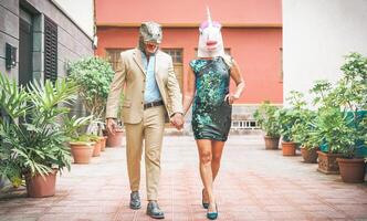 loco mayor Pareja vistiendo dinosaurio y unicornio máscara - maduro de moda personas teniendo divertido enmascarado a carnaval desfile - absurdo, excéntrico, surrealista, fest y gracioso mascarada concepto foto