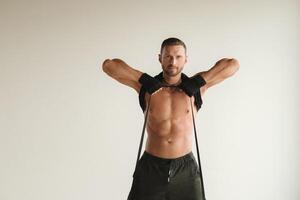 A man with a naked torso is engaged in strength fitness using a rubber loop indoors photo