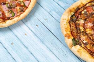 Two different delicious big pizzas on a blue wooden background photo