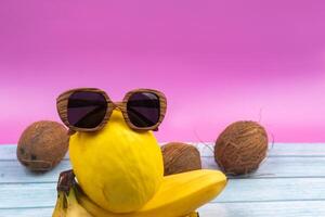 An assortment of yellow fruits and glasses lies on a pink background photo