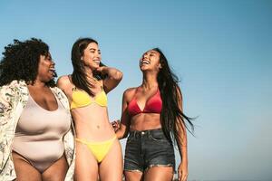 Happy multiracial females with different body size having fun walking on the beach during summer holidays photo