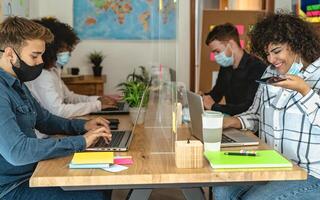 Young multiracial people using computer in co-working creative space while wearing face mask - Health and business technology concept photo