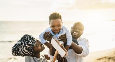 Happy African family having fun on the beach during summer vacation - Parents love and unity concept photo
