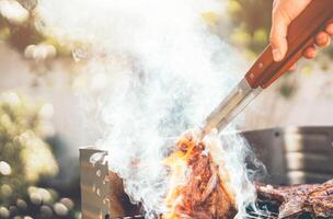 Man chef grilling beef steak at barbecue dinner party outdoor - Close up male hand cooking meat on bbq for family in the garden - Food, weekend activities and people lifestyle concept photo