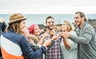 Happy group of friends celebrating with sparkling stars fireworks outdoor - People having fun enjoying a moment together next the ocean - Concept of friendship, youth, party photo