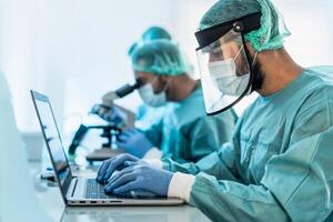 Doctors working in research laboratory using computer and examining microorganisms through microscope - Science and technology concept photo