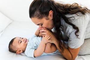 contento madre teniendo divertido con su pequeño bebé en cama - familia y maternidad concepto foto