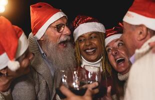 Happy senior friends celebrating Christmas holidays toasting with red wine glasses on house patio party photo