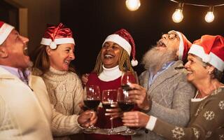 Happy senior friends celebrating Christmas holidays while toasting with red wine glasses on house patio party photo