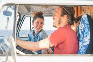 Happy couple inside a vintage minivan making a roadtrip - Travelers driving next to the coast with a van camper - Vacation, love, travel lifestyle concept photo