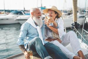 Senior couple toasting champagne on sailboat vacation - Happy elderly people having fun celebrating wedding anniversary on boat trip - Love relationship and travel lifestyle concept photo