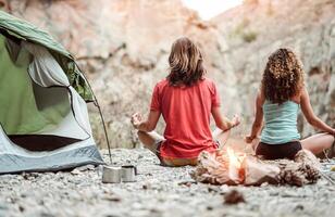 Young couple meditating together while camping on mountains - Healthy people training mind with meditate exercises - Youth expression culture and health lifestyle concept photo