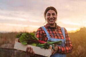 Happy female farmer holding a wood box containing fresh vegetables photo