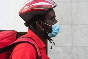 African rider man delivering meal to customers with electric scooter while wearing face mask during corona virus outbreak - Ecological fast delivery food concept photo