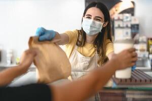 bar propietario trabajando solamente con tomar lejos pedidos durante corona virus brote - joven mujer trabajador vistiendo cara quirúrgico máscara dando eliminar comida a clientes - cuidado de la salud y comida bebida concepto foto