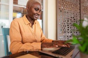 African woman working on laptop in bar restaurant - Afro female typing on computer - Digital nomad and freelance lifestyle concept photo