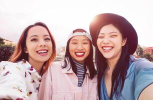 Happy Asian girls taking selfie with mobile smartphone outdoor - Young social friends having fun taking self photos outside - People, millennial generation and youth lifestyle concept