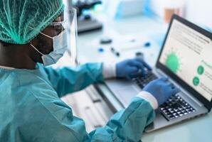 Medical worker wearing personal protective equipment using computer inside clinic during corona virus outbreak - Research and development concept photo