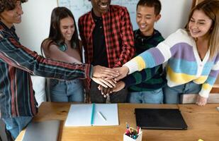 joven multirracial equipo de estudiantes poniendo su manos juntos mientras estudiando en salón de clases - trabajo en equipo y unidad concepto foto