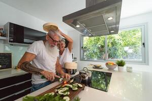 Happy senior couple having fun cooking together at home - Elderly people preparing health lunch in modern kitchen - Retired lifestyle family time and food nutrition concept photo