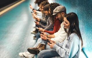 joven personas utilizando móvil teléfono inteligente mientras sentado en subterraneo esperando tren - juventud milenario fanático a nuevo tecnología concepto foto