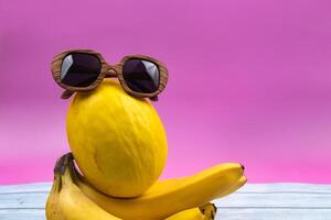 An assortment of yellow fruits and glasses lies on a pink background photo