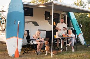 A happy family is resting nearby near their motorhome in the forest photo