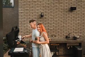 A married couple cooks grilled meat together on their terrace photo