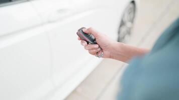 mujer abre un coche puerta con un remoto controlar llave. un mujer mano prensas en un coche alarma sistema en el antecedentes de un estacionado coche. torneado apagado el coche alarma video