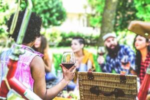 grupo de amigos haciendo un picnic en un jardín al aire libre - contento joven personas teniendo un divertido reunión con comida y rojo vino sentado en césped en un parque - amistad, juventud, estilo de vida concepto foto