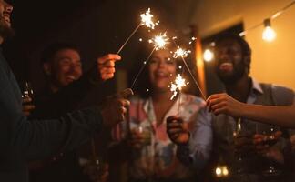 Happy young friends celebrating new year eve with sparklers fireworks and drinking cocktails on patio house party - Youth people lifestyle and holidays concept photo