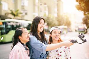 Happy Asian girls making video stories in the city center - Trendy young friends filming with gimbal smartphone  outdoor - Friendship, technology, youth people lifestyle and social media concept photo