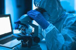 joven científico trabajando en laboratorio examinando coronavirus mediante microscopio - Ciencias y tecnología concepto foto