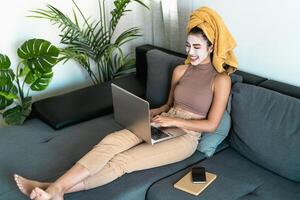 Young woman using laptop while having skin care day at home photo