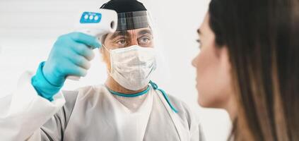 Doctor measuring temperature with new digital thermometer to young woman patient during corona virus pandemic - Health care and medical equipment concept photo